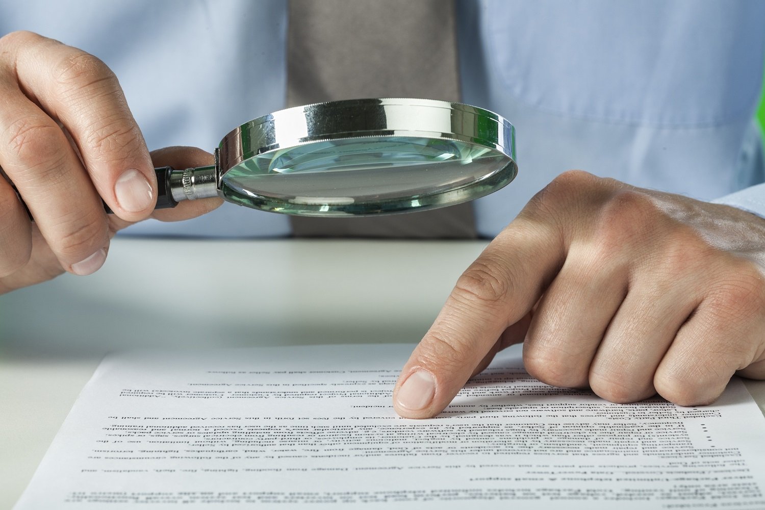 a pair of hands using magnifying glass over word document