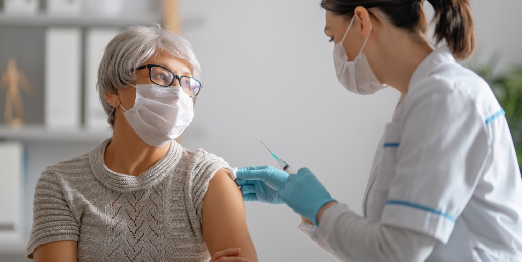 masked doctor holding vaccine next to masked patient's arm