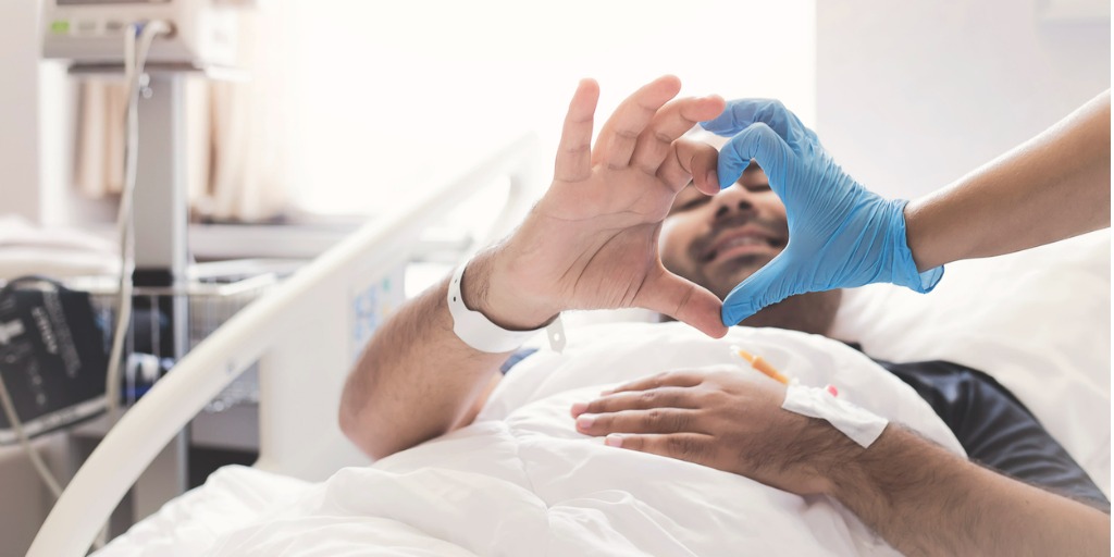 patient in bed making a heart with doctor's hand
