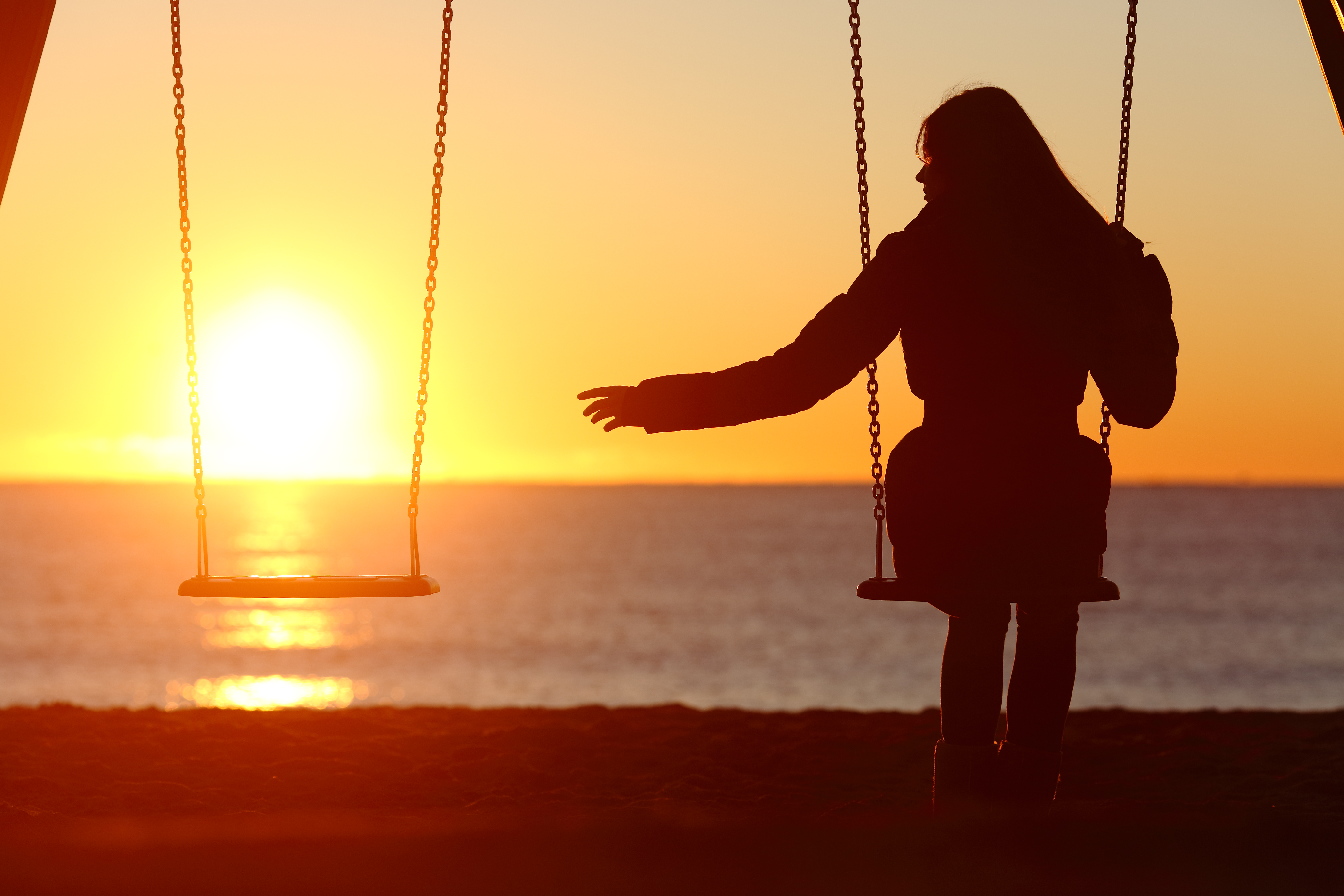 girl swinging next to empty swing in front of sunset