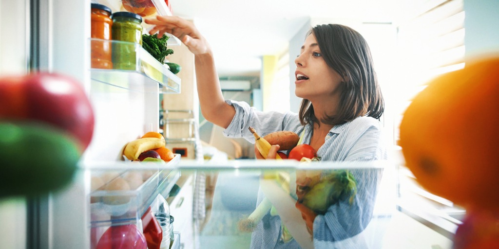 woman stocking refrigerator with fruits and vegetables